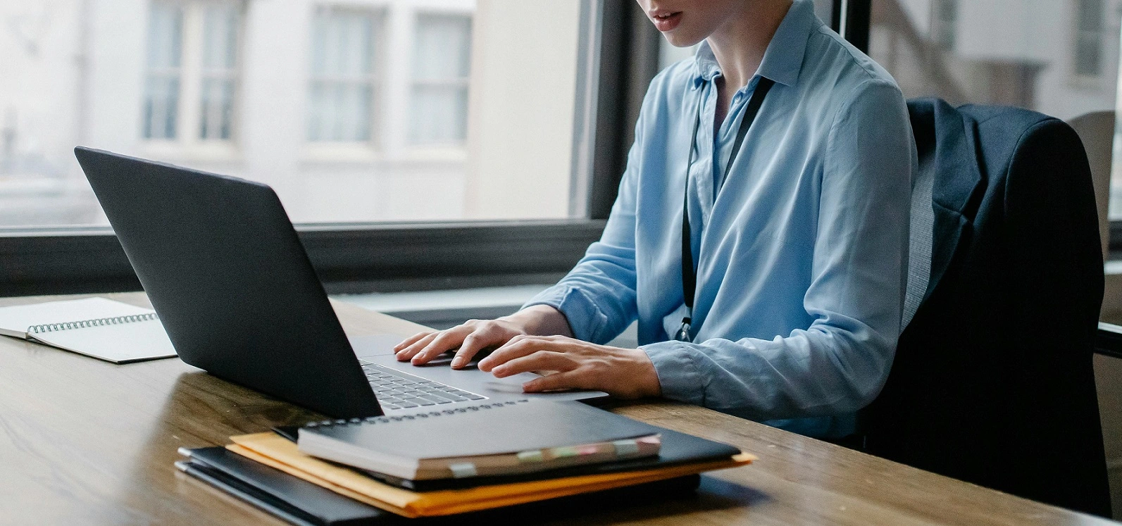Mulher sentada em uma mesa utilizando um organizador de notas fiscais em um computador
